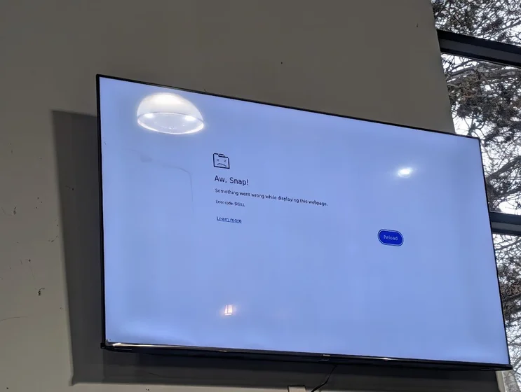 A TV on the wall inside a gym. It shows a Chromium crashed tab screen that reads:

Aw, Snap!
Something went wrong while displaying this webpage.
Error code: SIGILL
[Learn more]
[Reload]