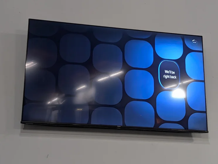 A TV hangs on the wall showing the Google TV Freeplay channel “We’ll be right back” waiting screen.